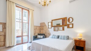 Una camera da letto con un letto, una sedia, un comodino e un'ampia finestra con tende.