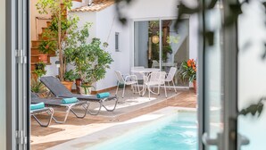 Area piscina con lettini, un tavolo con sedie e piante in vaso.