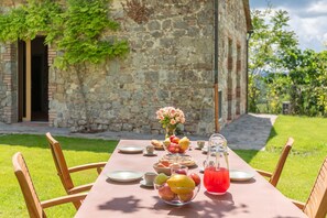 Un tavolo apparecchiato all'aperto con frutta, una brocca di bevanda rossa e un vaso di fiori.