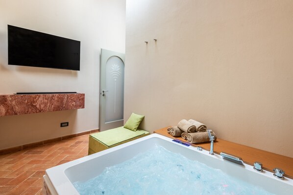 Un bagno con vasca, una TV montata a parete, un appendi asciugamani e una porta con pomello decorativo.