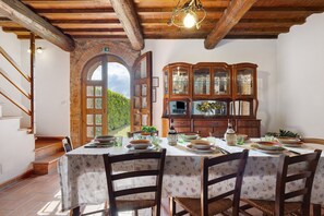 A dining area with a table set for four, wooden chairs, a cabinet with glass doors, and a staircase leading to an outdoor area. - Holiday Home 'Toscana' with Shared Pool, Private Garden and Wi-Fi (Colle di Val d'Elsa)