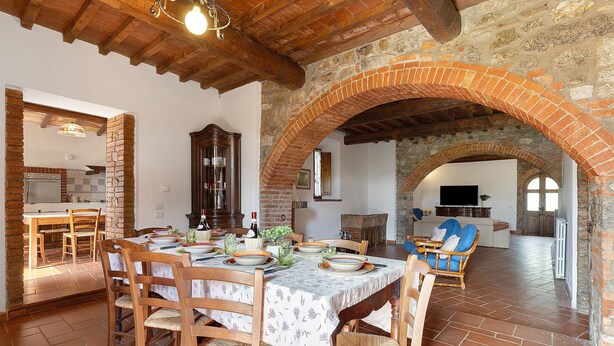A dining area with a brick archway, wooden chairs, a table set for four, and a television in the background. - Holiday Home 'Toscana' with Shared Pool, Private Garden and Wi-Fi (Colle di Val d'Elsa)