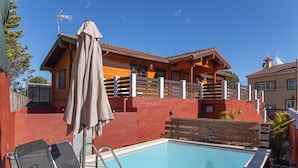 Una casa de madera con piscina, un patio cubierto y un área cercada.