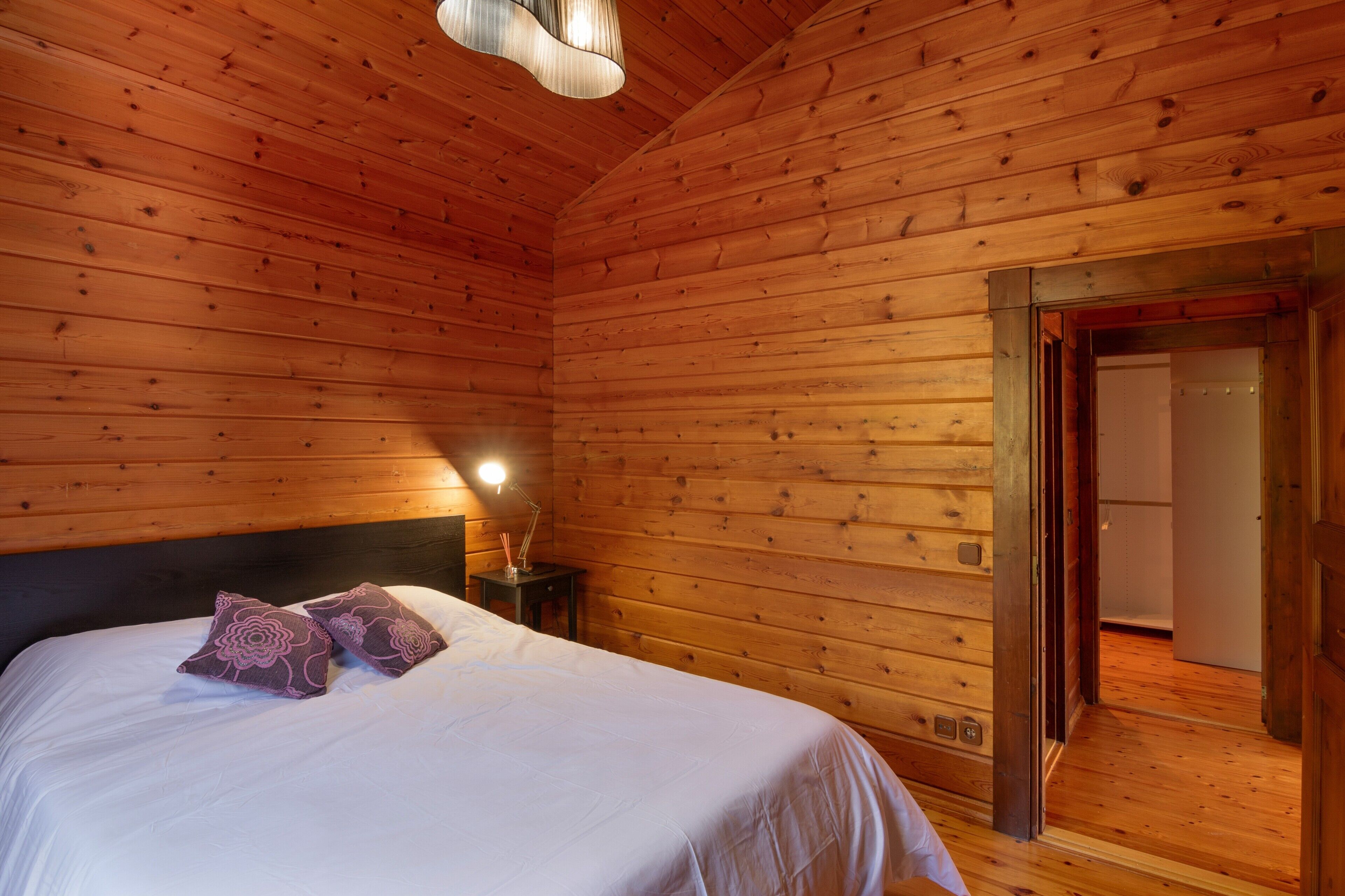 Una habitación con paneles de madera, una cama, una mesita de noche y una puerta que da a otra habitación.