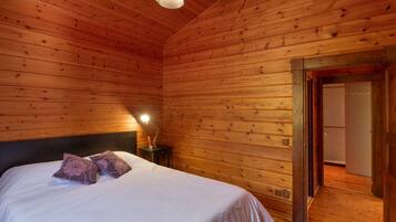 Una habitación con paneles de madera, una cama, una mesita de noche y una puerta que da a otra habitación.