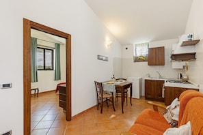 A compact kitchen with a dining area, a sofa, and a window with curtains. - Cottage 'Nel Verde Con Jacuzzi' with Shared Pool and Shared Garden (Colle di Val d'Elsa)