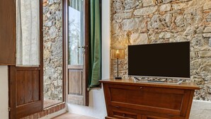 A room with a stone wall, wooden furniture, and a television on a stand. - Cottage 'Nel Verde Con Jacuzzi' with Shared Pool and Shared Garden (Colle di Val d'Elsa)
