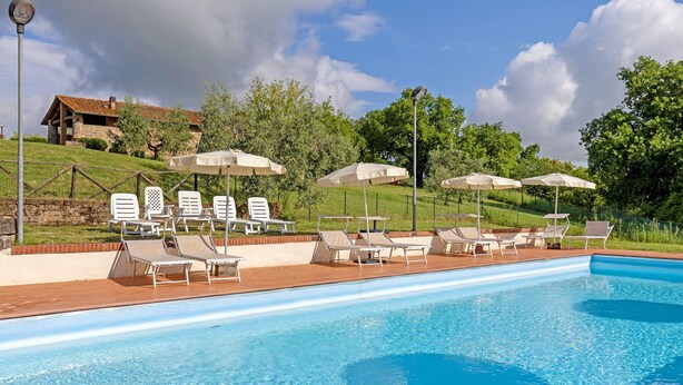 A swimming pool with lounge chairs and umbrellas, surrounded by a fence and greenery. - Cottage 'Nel Verde Con Jacuzzi' with Shared Pool and Shared Garden (Colle di Val d'Elsa)
