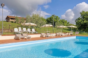 A swimming pool with lounge chairs and umbrellas, surrounded by a fence and greenery.