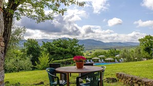 A round table with chairs, a potted plant, and a view of mountains and a pool in the background. - Cottage 'Nel Verde Con Jacuzzi' with Shared Pool and Shared Garden (Colle di Val d'Elsa)