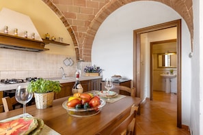 A kitchen with a brick archway, wooden cabinets, a dining table with a fruit bowl, a wine glass, and a bottle. - Cottage 'Rustico Toscano' with Shared Pool, Shared Garden and Wi-Fi (Colle di Val d'Elsa)
