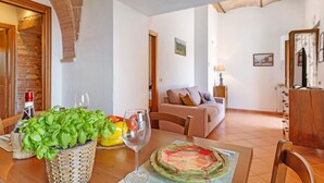 A dining area with a table set for two, a woven basket with green leaves, a wine glass, and a fruit bowl.