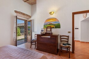 A room with a bed, a wooden dresser, a chair, a wall-mounted light, and a door leading outside. - Cottage 'Rustico Toscano' with Shared Pool, Shared Garden and Wi-Fi (Colle di Val d'Elsa)