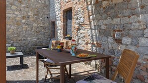 An outdoor patio with a stone wall, a wooden table, chairs, and a window.