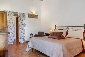 A bedroom with a bed, a chair, a nightstand, a lamp, and a wall-mounted light fixture. - Cottage 'Rustico Toscano' with Shared Pool, Shared Garden and Wi-Fi (Colle di Val d'Elsa)