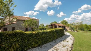 A stone building with a tiled roof, a hedge, and a gravel path.