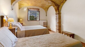A bedroom with two beds, a window, a lamp, and an arched brick ceiling.