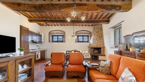 A rustic living room with exposed wooden beams, a fireplace, and a sofa with orange cushions.