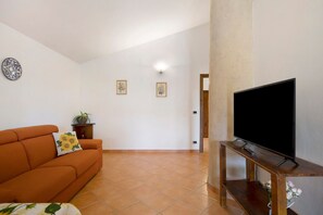 Een woonkamer met een bank, een televisie op een houten dressoir, en een betegelde vloer.