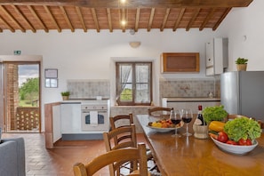 A kitchen with a wooden ceiling, a dining table with chairs, a refrigerator, and a window with curtains.