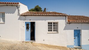Un edificio blanco con techo de tejas, una puerta azul y una ventana.