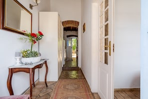 Un corridoio con una porta bianca, uno specchio, un vaso con fiori rossi e un tappeto decorato.