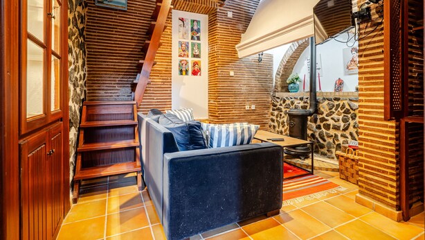 Un interior acogedor con una escalera, un sofá, zona de comedor y una pared de piedra.
