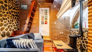 Una habitación acogedora con pared de piedra, escalera de madera, sofá y una mesa.