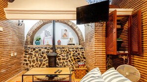 Una habitación acogedora con pared de piedra, chimenea, televisor y sofá con cojines a rayas.