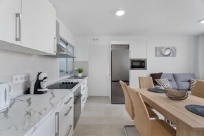 A modern kitchen with white cabinetry, a built-in oven, and a dining area with a wooden table and chairs.