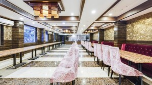 A spacious restaurant with long tables and benches, high ceilings with decorative lighting, and a modern interior design. - Luxury Urban Stays Near Chennai Airport (Chennai)