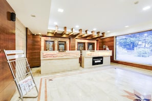 A reception area with a marble counter, wooden accents, and a view of a temple through a large window. - Luxury Urban Stays Near Chennai Airport (Chennai)