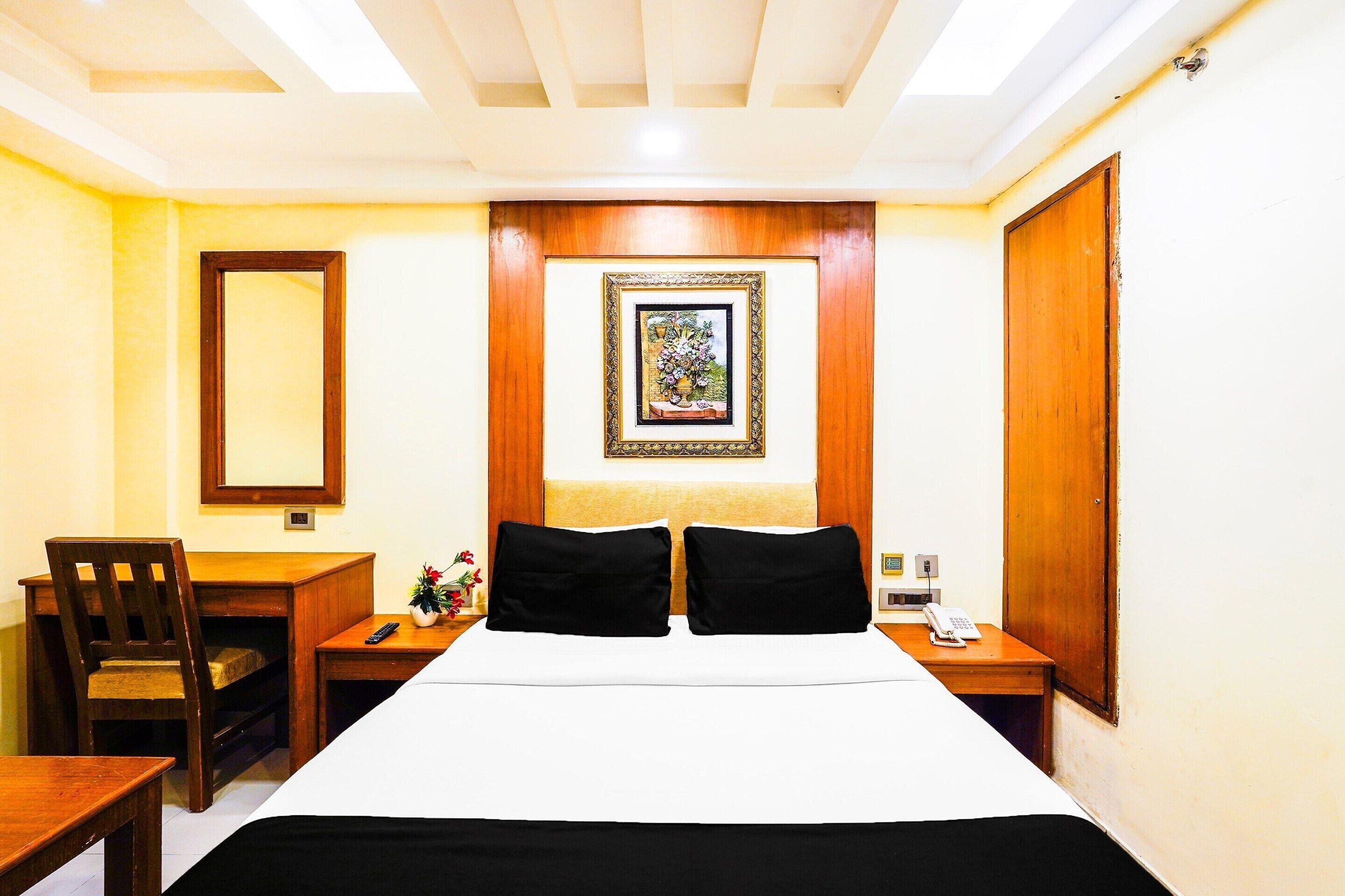 Une chambre d’hôtel comprenant un lit, un bureau, une chaise, une table de chevet, un téléphone et un tableau encadré au mur.