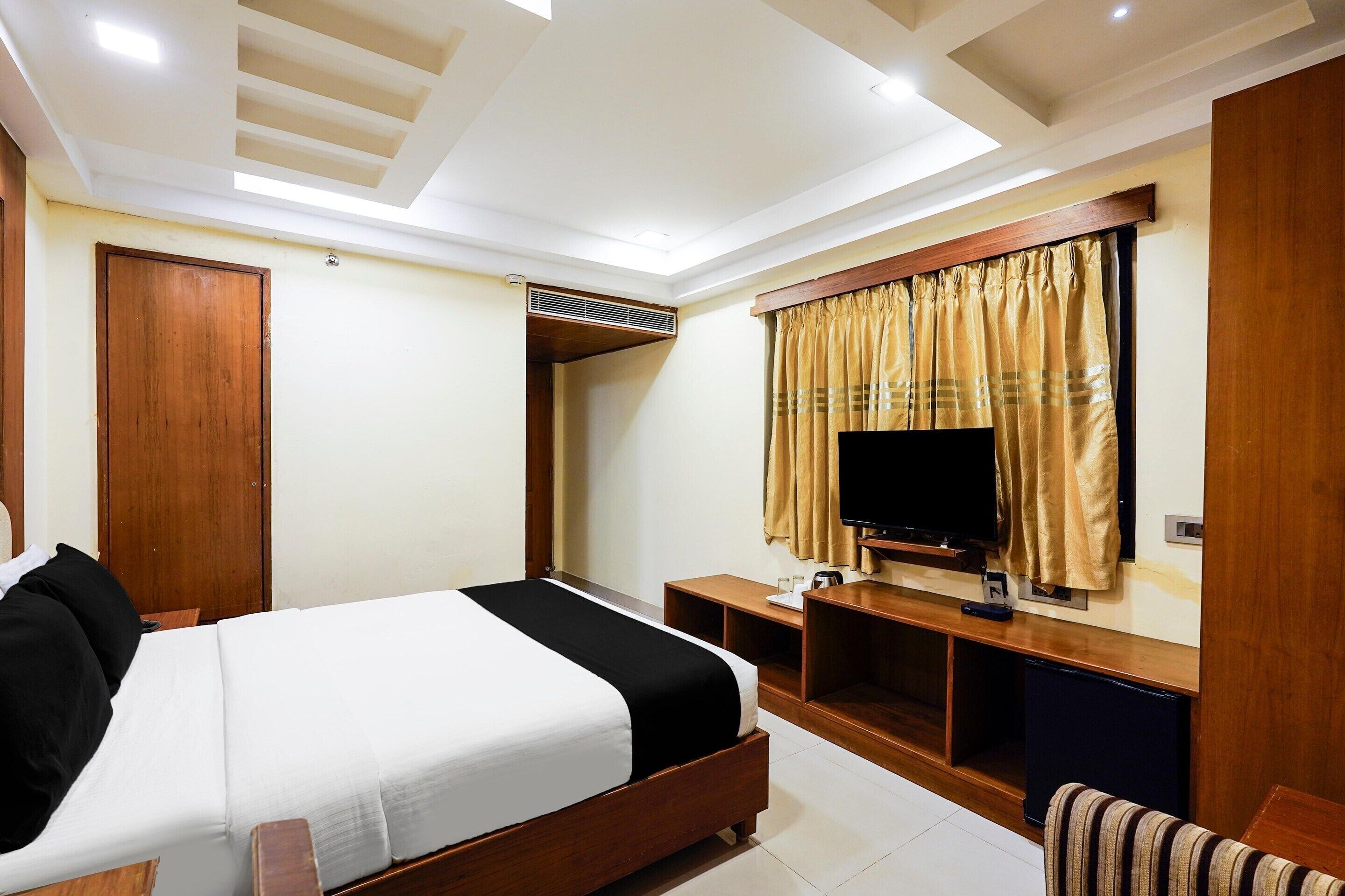 A hotel room with a bed, a TV, a wooden wardrobe, a desk, and a window with curtains.