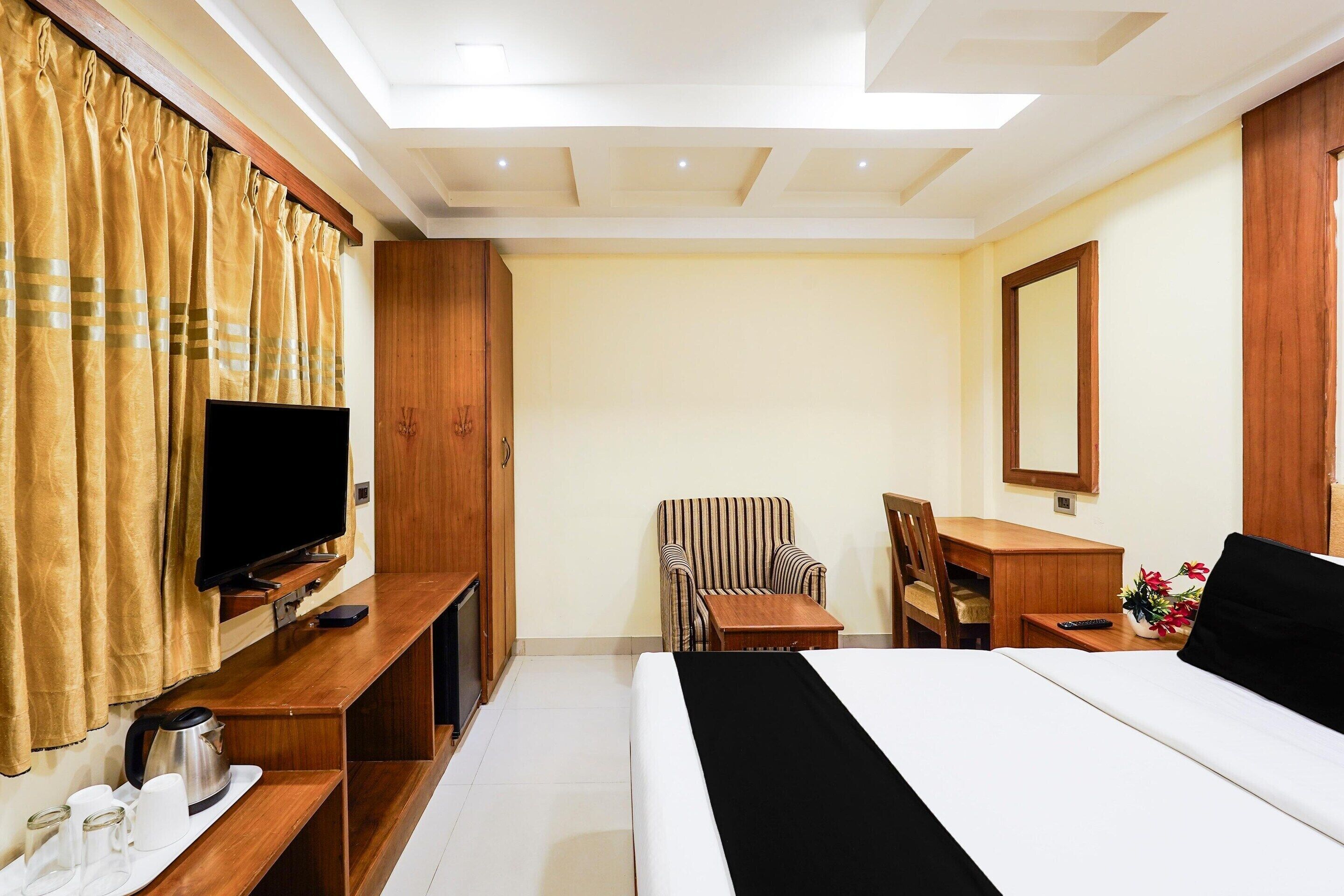 A hotel room with a bed, a desk, a chair, a television, and a mirror.