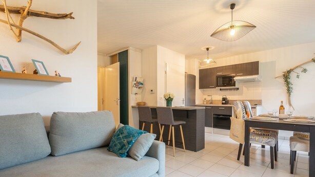 A modern living room with a grey sofa, a dining area with a table and chairs, and a kitchen with dark cabinets and a microwave. - Les Jardins d'Aunis by Interhome (Royan)