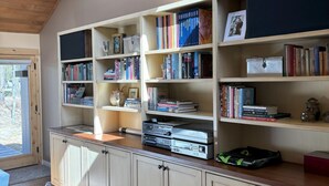 A spacious room with a large wooden bookshelf filled with books and DVDs, a wooden desk, and a comfortable seating area with a sofa and a rug. - Meadow House 64 in Sunriver w/ Golf Course & Mt View, WiFi, AC, Hot Tub (Sunriver)