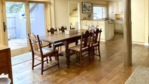 A spacious dining area with a large wooden table and chairs, a kitchen in the background, and a view of the backyard through large sliding glass doors. - Meadow House 64 in Sunriver w/ Golf Course & Mt View, WiFi, AC, Hot Tub (Sunriver)