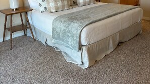 A neatly made bed with a checkered pillow set, two bedside lamps, a wooden nightstand, and a bathroom visible in the background. - Meadow House 64 in Sunriver w/ Golf Course & Mt View, WiFi, AC, Hot Tub (Sunriver)