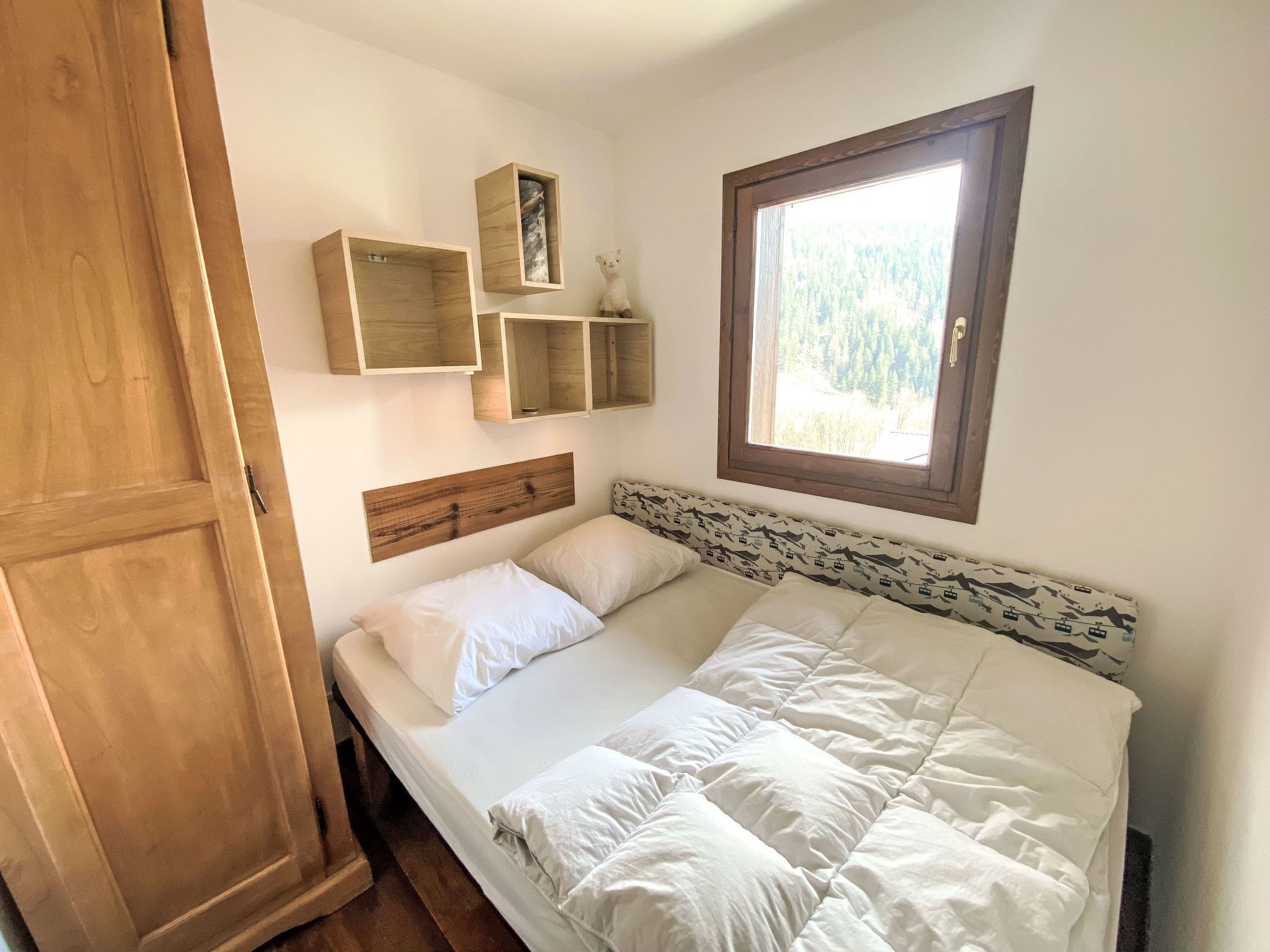 A bedroom with a wooden headboard, a bed with white bedding, and built-in wooden shelves above the bed.