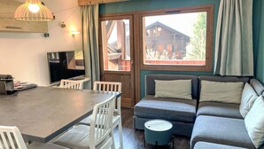 Ein gemütliches Wohnzimmer mit Essbereich, einer Couch, einem Fernseher und einem Fenster mit Blick auf ein Holzhaus.