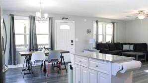 A modern kitchen with white cabinets, a dining area with a table and chairs, a sofa, and a ceiling fan. - Ventures in Leicester (Leicester)