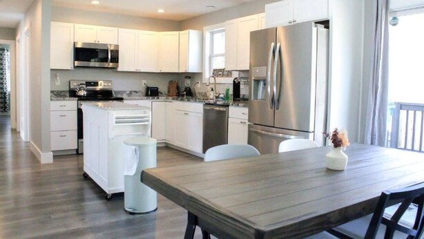 A modern kitchen with white cabinets, stainless steel appliances, and a wooden dining table. - Ventures in Leicester (Leicester)