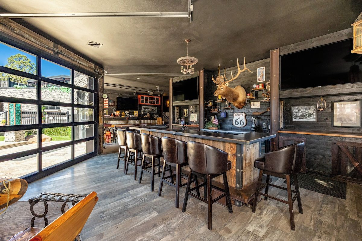 Een barruimte met een groot raam, een opgeplakt hertenhoofd en een bar met krukken.