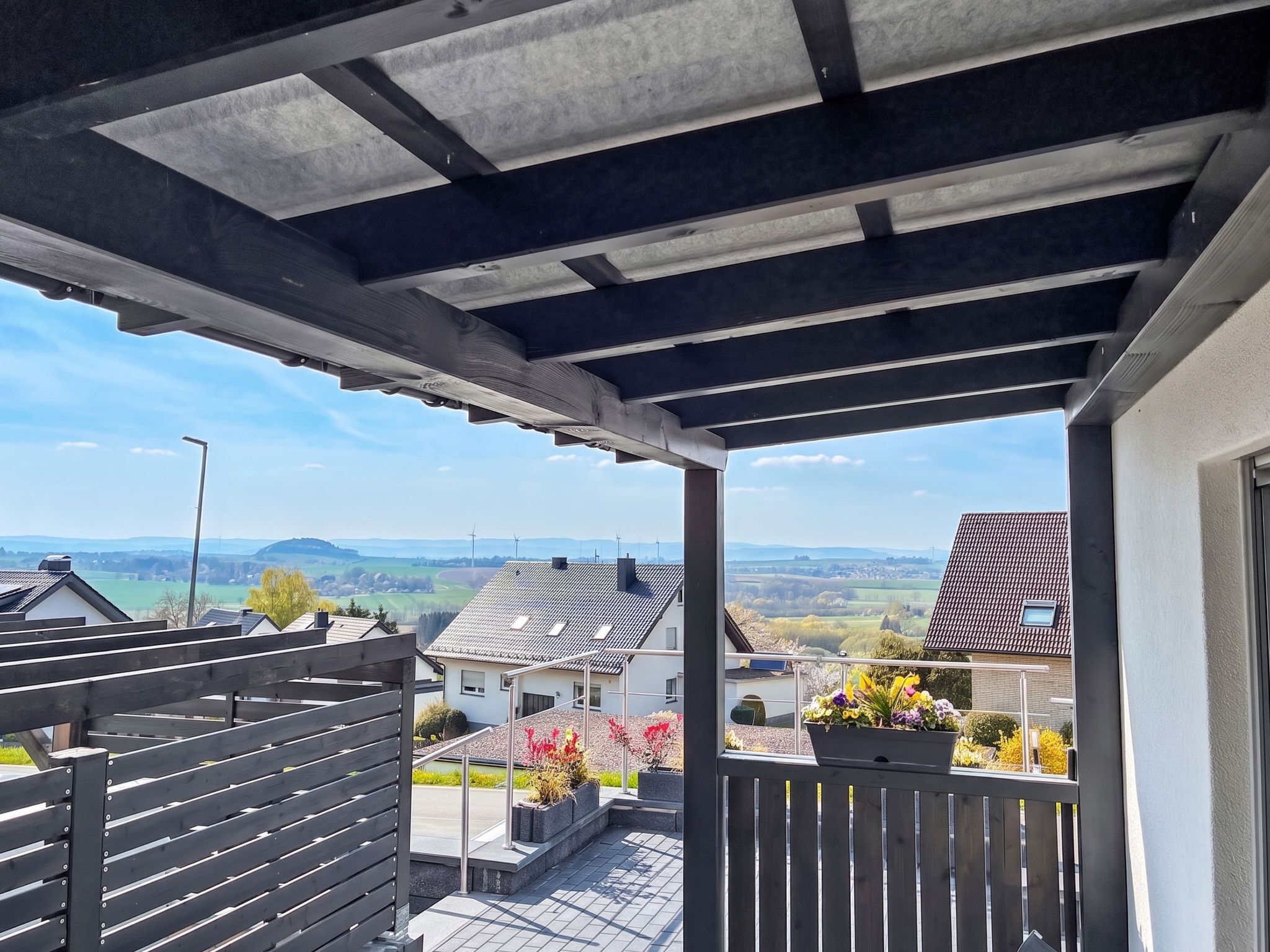 Un balcón con vistas a una zona residencial, que incluye casas y un paisaje montañoso.