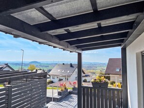 Un balcon donnant sur un quartier résidentiel, avec des maisons et un paysage vallonné.