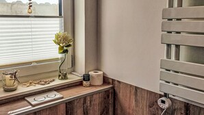 Ein Badezimmer mit Fenster, Toilettenpapierrolle, einer kleinen Pflanze und einem dekorativen Gegenstand auf der Ablagefläche.