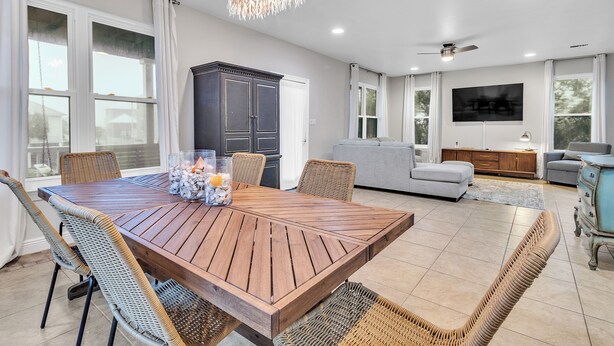 A spacious living area with a wooden dining table, wicker chairs, a dark cabinet, a grey sofa, and a television mounted on the wall. - Pet Friendly- Fort Morgan | Sleeps 12 | 3BR | 2.5BA (Gulf Shores)