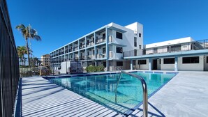 A modern hotel with a pool area, featuring a wooden deck and a clear blue pool.