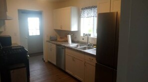 A kitchen with white cabinets, a refrigerator, a sink, and a window with a curtain.
